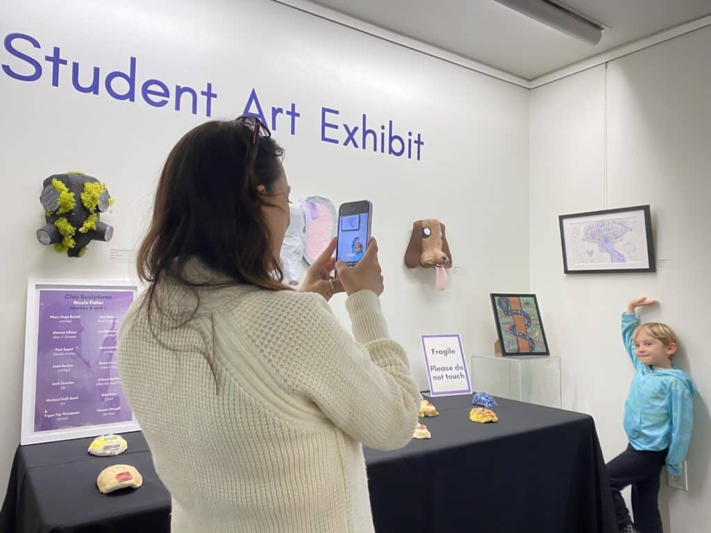 Malibu resident Gina Longo takes a photo of her son Leo Gigliotti posing with his drawing Happy Colors at the 2023 Student Art Exhibit reception on Feb 26